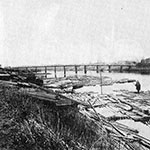 「（第2次）六郷橋」（明治7年建造。「左内橋」とも）。手前は筏の溜まり場。洪水時、筏が暴れて橋を壊すことも　※「パブリックドメインの写真（根拠→）」を使用　出典：『大田区史（下）』　原典：「SIGHTS AND SCENES ON THE TOKAIDOO」